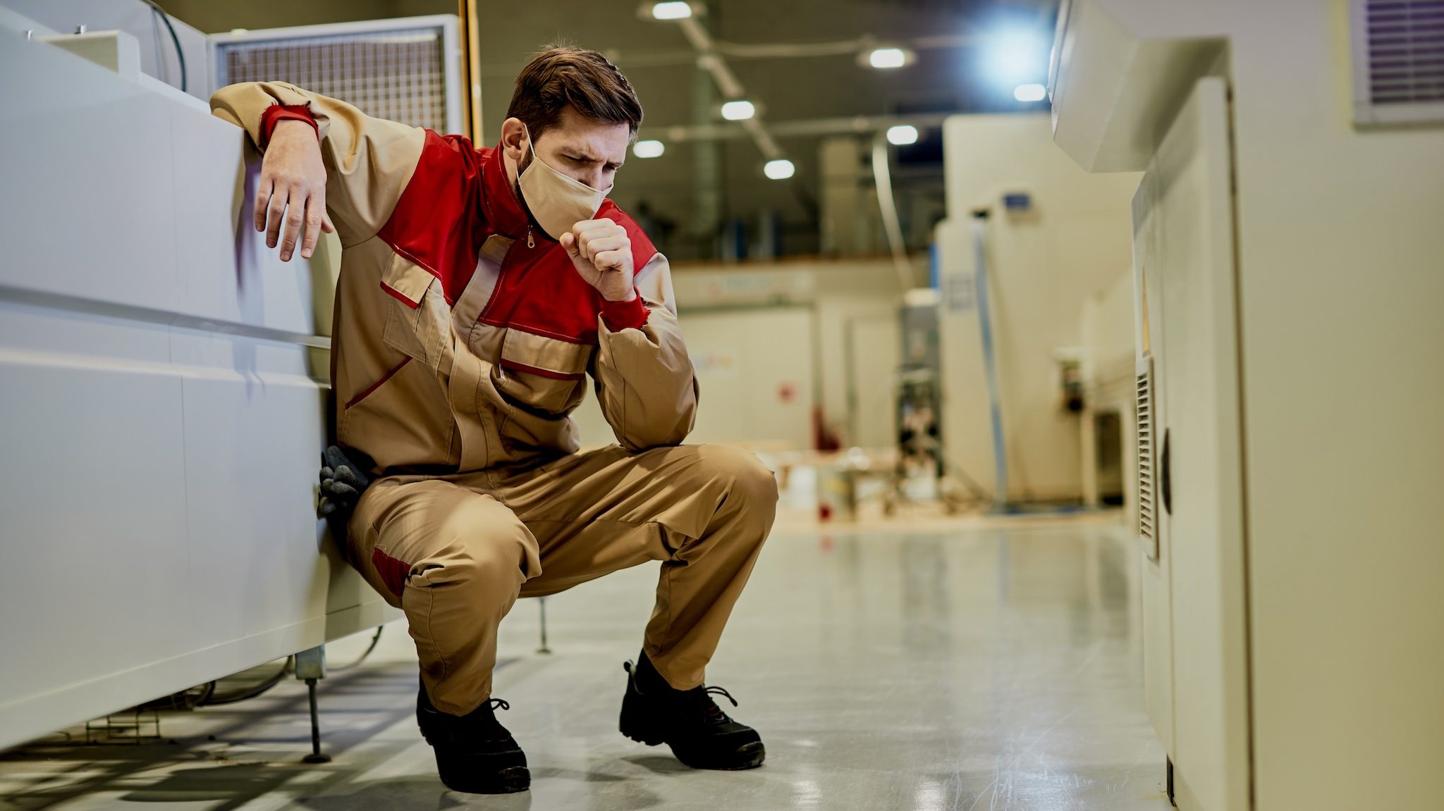 Fabriksarbetare med munskydd hostar på grund av dålig luftkvalitet, damm och kemikalier. Dammbindning med luftfuktning är den säkraste lösningen.